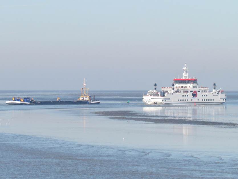 Een baggerschip en veerboot passeren elkaar op de Waddenzee in de vaargeul naar Ameland
