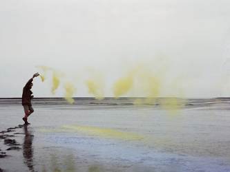 Kunstenaar Han Jansen strooit geel pigment in de Waddenzee voor een tijdelijk kunstwerk. Foto John Stoel