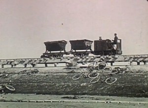 Een locomotief met kiepkarren rijdt over de strekdam bij Paesens, jaren '50. Still uit de film 'Van waddenzand tot vruchtbaar land'. 